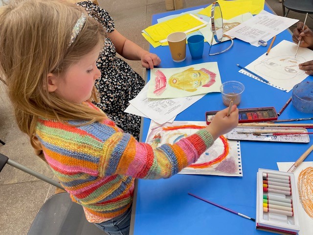 A primary school aged girl in a rainbow coloured jumper painting with water colours.