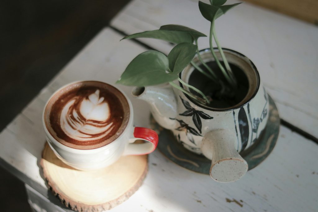 On the right is a teapot used to grow a plant. On the left is a cup of coffee with latte art.